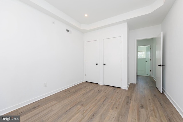 unfurnished bedroom with light hardwood / wood-style flooring and a tray ceiling