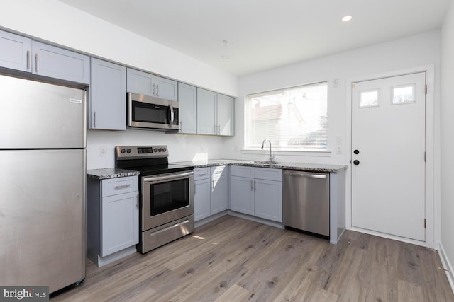 kitchen with light hardwood / wood-style floors, light stone counters, appliances with stainless steel finishes, and gray cabinets