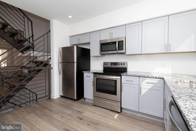 kitchen featuring light wood-type flooring, stainless steel appliances, and light stone countertops