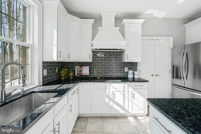 kitchen featuring sink, stainless steel refrigerator with ice dispenser, premium range hood, and plenty of natural light