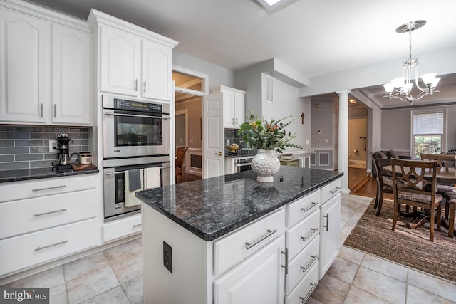 kitchen featuring white cabinetry, backsplash, a kitchen island, double oven, and ornate columns