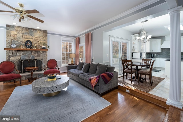 living room with a fireplace, wood-type flooring, ornate columns, and ceiling fan with notable chandelier