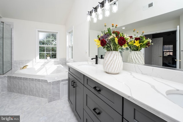 bathroom featuring vanity, vaulted ceiling, and tiled tub