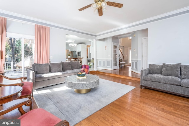 living room with hardwood / wood-style floors, ornamental molding, and ceiling fan with notable chandelier