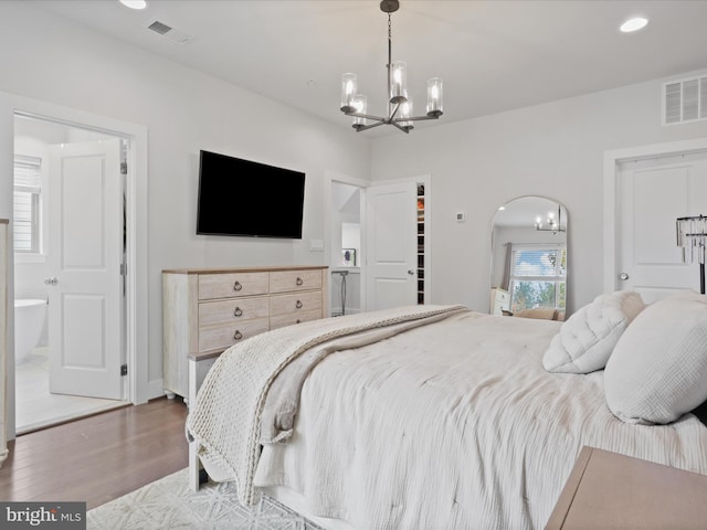 bedroom with a spacious closet, connected bathroom, hardwood / wood-style flooring, and an inviting chandelier