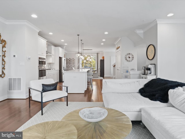 living room featuring sink, crown molding, dark hardwood / wood-style floors, and a chandelier