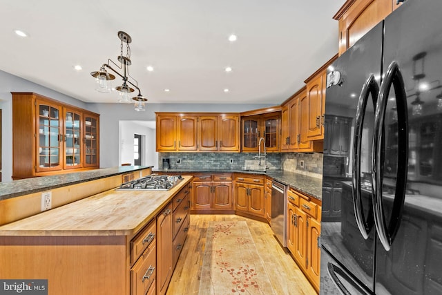 kitchen with tasteful backsplash, appliances with stainless steel finishes, butcher block countertops, light hardwood / wood-style floors, and decorative light fixtures