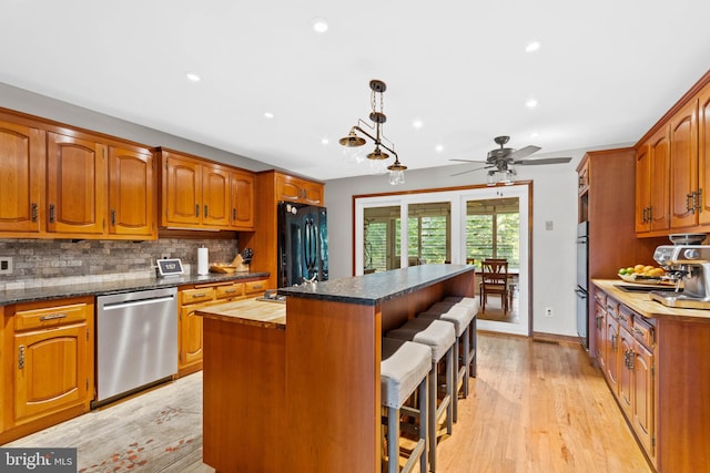 kitchen with tasteful backsplash, appliances with stainless steel finishes, light wood-type flooring, a kitchen island, and pendant lighting