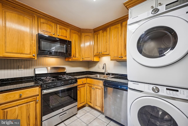 kitchen with stacked washer and dryer, light tile patterned floors, appliances with stainless steel finishes, dark stone countertops, and sink