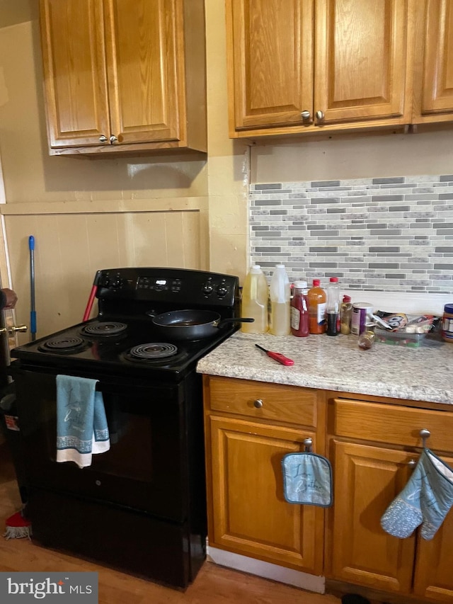 kitchen with black / electric stove, light hardwood / wood-style flooring, and tasteful backsplash