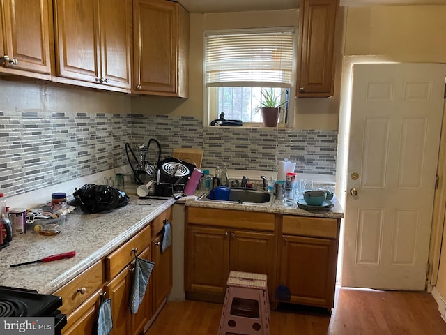 kitchen featuring decorative backsplash, black stove, light stone countertops, light wood-type flooring, and sink