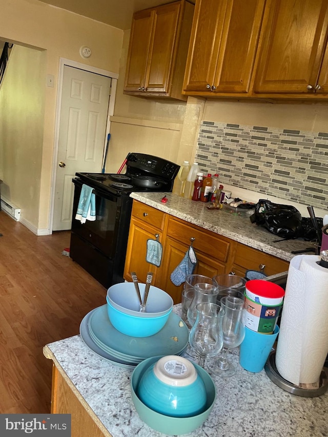 kitchen featuring baseboard heating, dark wood-type flooring, backsplash, black electric range, and light stone counters