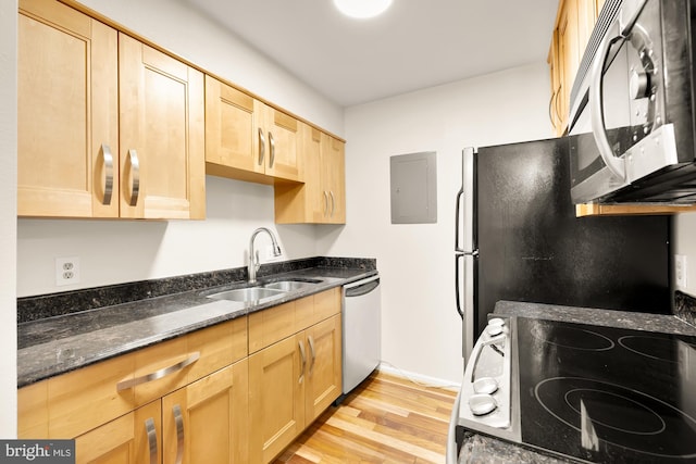 kitchen with electric panel, sink, dark stone countertops, light wood-type flooring, and appliances with stainless steel finishes