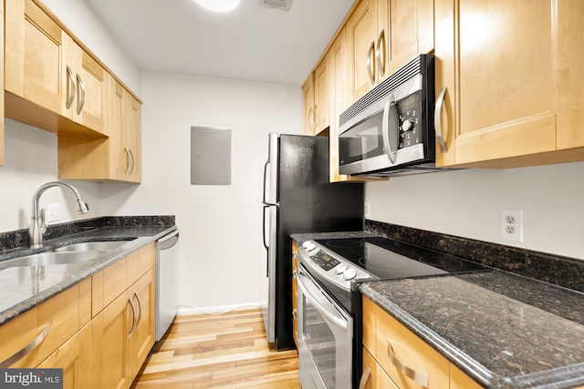 kitchen featuring appliances with stainless steel finishes, light wood-type flooring, dark stone counters, sink, and electric panel