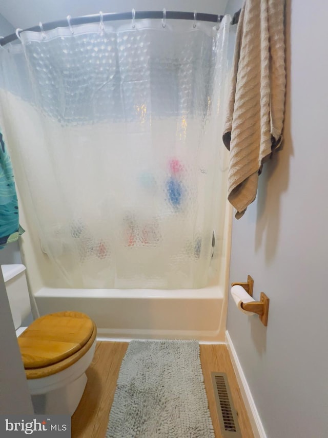 bathroom with hardwood / wood-style floors, toilet, and shower / tub combo with curtain