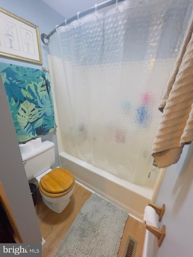 bathroom featuring hardwood / wood-style flooring, shower / tub combo with curtain, and toilet