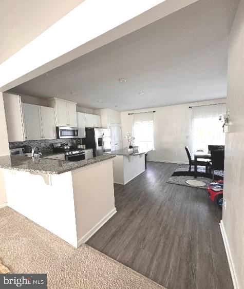 kitchen with appliances with stainless steel finishes, kitchen peninsula, white cabinetry, and dark hardwood / wood-style floors