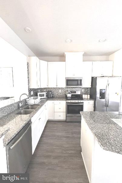 kitchen with sink, stainless steel appliances, white cabinets, dark wood-type flooring, and dark stone countertops