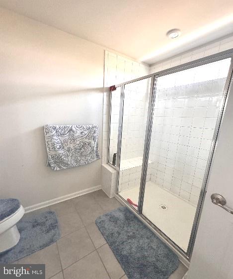 bathroom featuring a shower with door, toilet, and tile patterned flooring