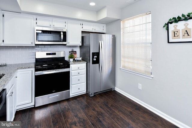 kitchen with appliances with stainless steel finishes, white cabinetry, dark wood-type flooring, light stone counters, and decorative backsplash