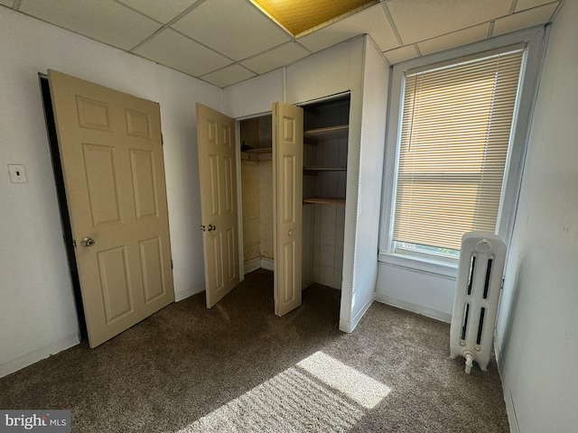 unfurnished bedroom featuring a closet, a drop ceiling, radiator heating unit, and carpet floors