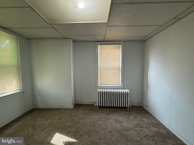 empty room with a drop ceiling, radiator heating unit, and carpet floors