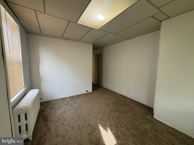 unfurnished room with a drop ceiling, radiator, and carpet