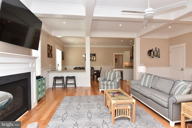 living room with light hardwood / wood-style floors, beamed ceiling, ornamental molding, ceiling fan, and coffered ceiling