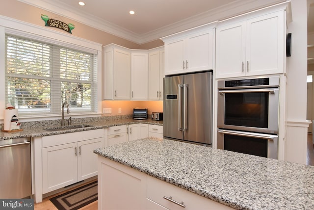 kitchen featuring stainless steel appliances, sink, light stone countertops, crown molding, and white cabinets