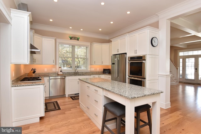 kitchen with white cabinets, light hardwood / wood-style floors, a kitchen island, and appliances with stainless steel finishes