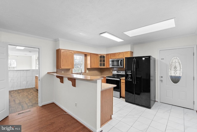 kitchen featuring stainless steel appliances, light hardwood / wood-style flooring, kitchen peninsula, a kitchen bar, and ornamental molding