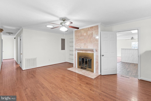 unfurnished living room with a textured ceiling, hardwood / wood-style flooring, built in features, electric panel, and a tiled fireplace