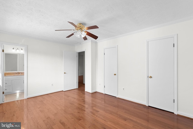 unfurnished bedroom featuring ensuite bath, ceiling fan, wood-type flooring, and a textured ceiling