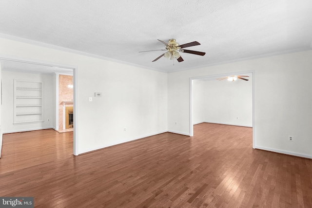 spare room featuring hardwood / wood-style flooring, built in shelves, a fireplace, and a textured ceiling