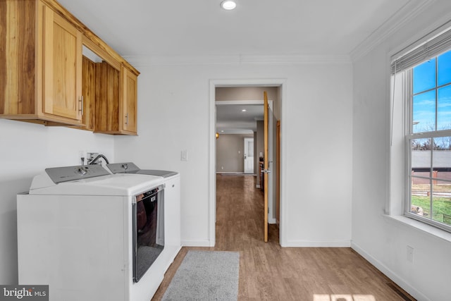 clothes washing area with baseboards, washing machine and dryer, light wood-type flooring, ornamental molding, and cabinet space