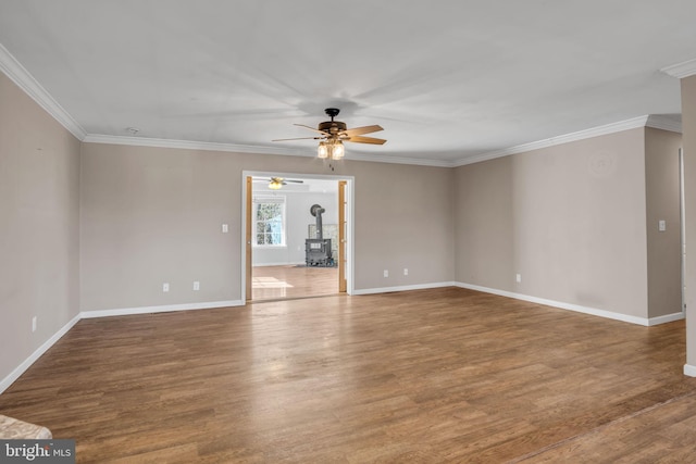 unfurnished room with crown molding, a wood stove, wood finished floors, and baseboards