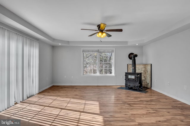 unfurnished living room with a ceiling fan, a wood stove, wood finished floors, and baseboards