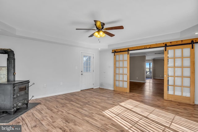 unfurnished living room featuring a barn door, a wood stove, wood finished floors, and ceiling fan