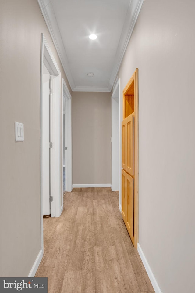 hallway featuring baseboards, ornamental molding, and light wood finished floors