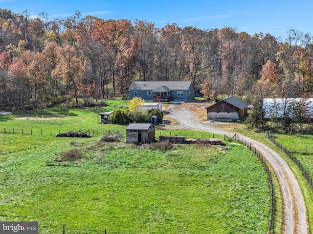 view of yard featuring a rural view, a forest view, fence, an outdoor structure, and driveway