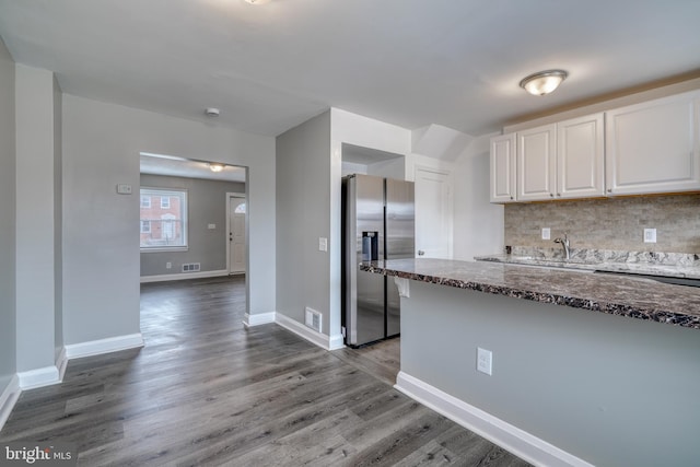 kitchen with white cabinets, hardwood / wood-style flooring, backsplash, dark stone countertops, and stainless steel fridge