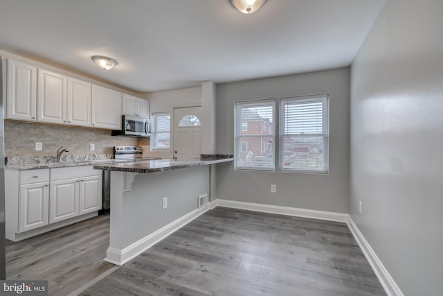 kitchen featuring white cabinetry, kitchen peninsula, stainless steel appliances, and light hardwood / wood-style floors