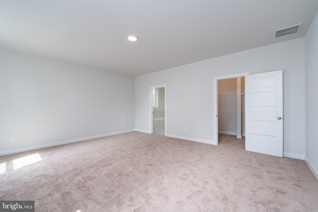 unfurnished bedroom with ensuite bathroom, light colored carpet, a walk in closet, and a closet