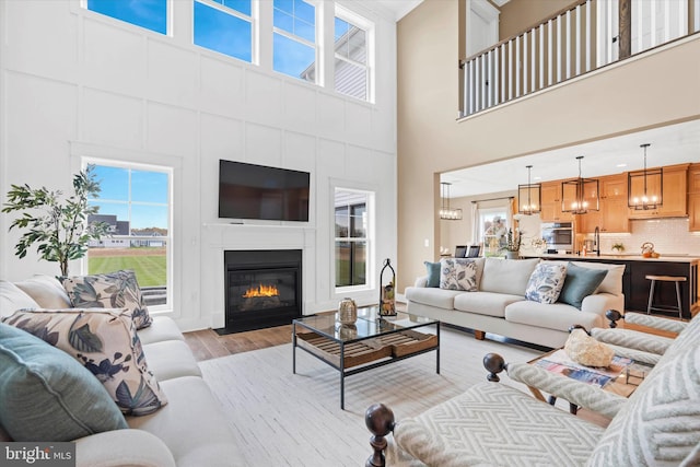 living room with sink, light hardwood / wood-style floors, a high ceiling, and a chandelier