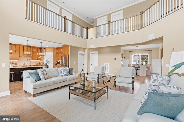 living room with crown molding, sink, a high ceiling, and light wood-type flooring