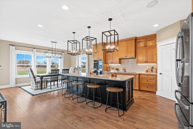 kitchen featuring a breakfast bar area, an island with sink, hanging light fixtures, stainless steel appliances, and dark hardwood / wood-style flooring