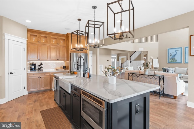 kitchen featuring light hardwood / wood-style flooring, decorative light fixtures, an island with sink, and light stone counters