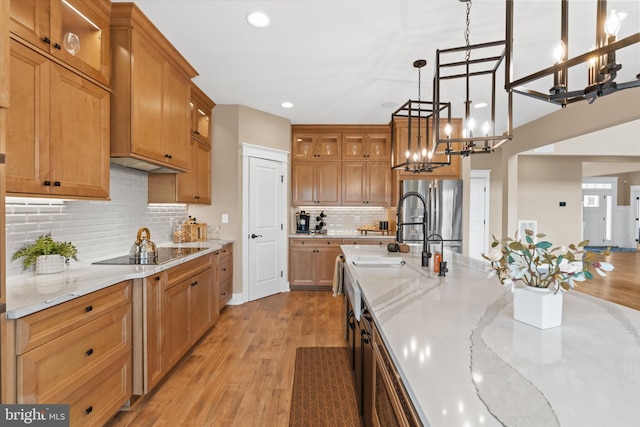 kitchen featuring black electric stovetop, decorative light fixtures, an inviting chandelier, light stone counters, and light hardwood / wood-style floors