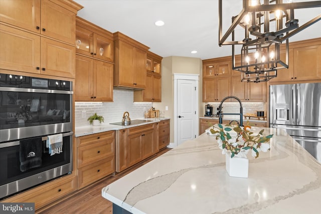 kitchen featuring light stone countertops, appliances with stainless steel finishes, pendant lighting, hardwood / wood-style flooring, and a chandelier