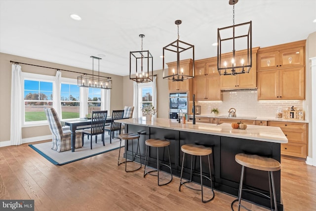 kitchen with a kitchen island with sink, double oven, cooktop, and light wood-type flooring